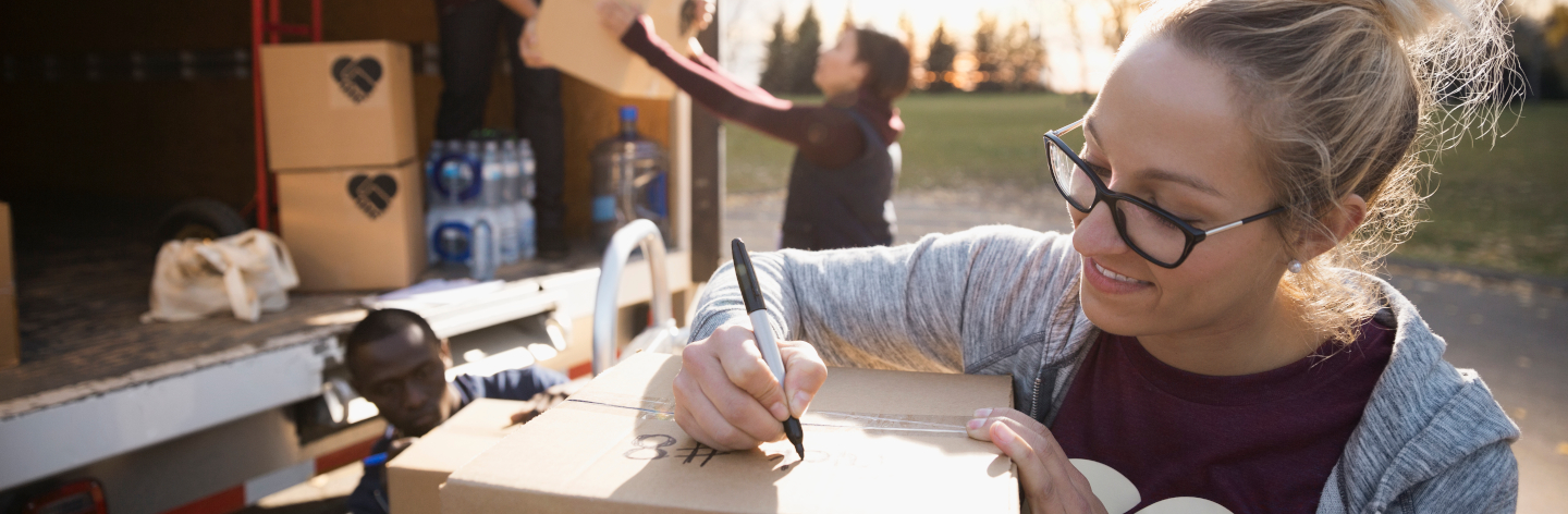 Female Volunteer Writing On Cardboard Box Outside Truck