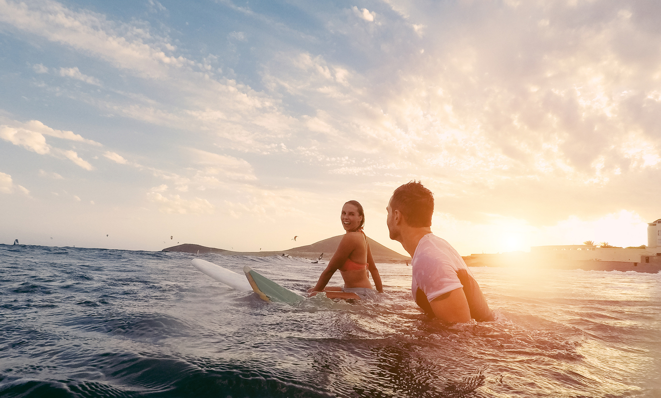 Fit Couple Surfing At Sunset Surfers Friends Having Fun Inside Ocean Extreme Sport And Vacation Concept Focus On Man Head Original Sun Color Tones