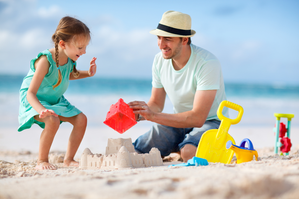 Father,and,daughter,on,beach,building,sand,castle